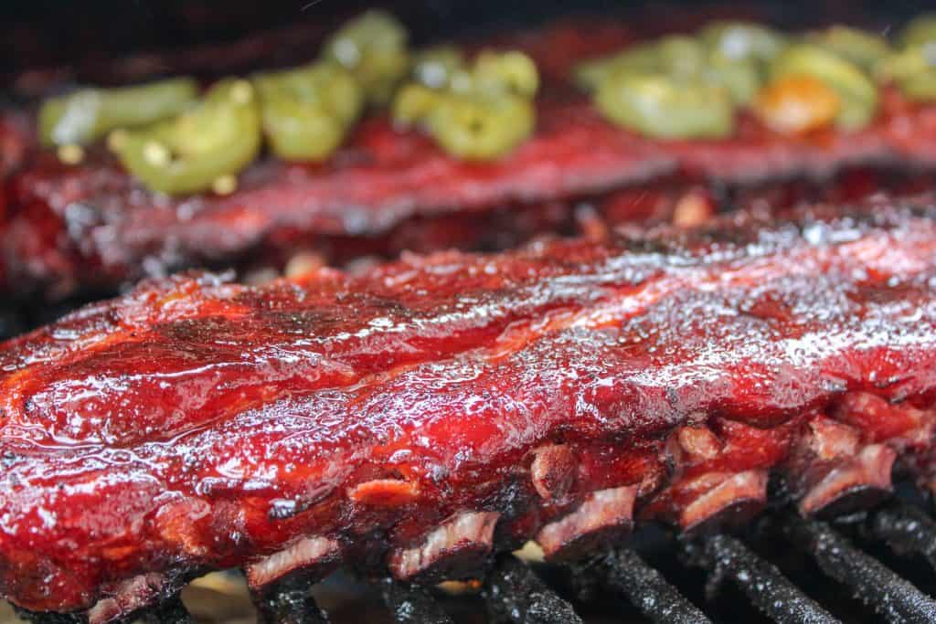 321 baby back ribs on a grill, ribs with jalapenos on top in the background - how to smoke ribs in an electric smoker