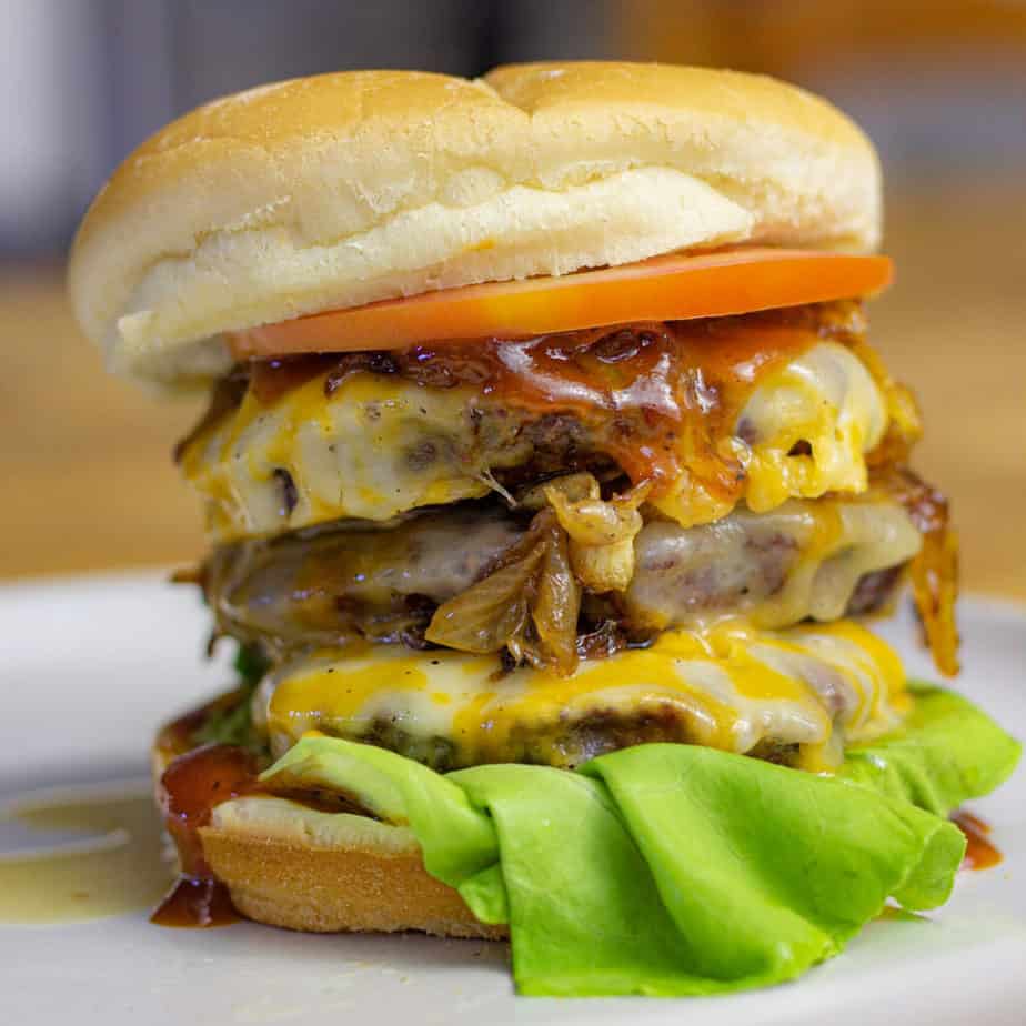 smoked triple cheeseburger on a bun with lettuce, tomato, and caramelized onions