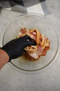 Bacon being mixed with syrup and brown sugar in bowl.