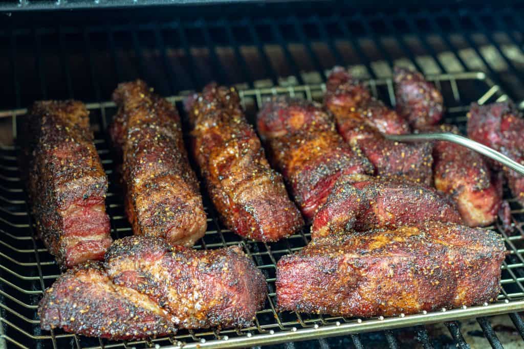 multiple strips of boneless country style ribs with rub in a smoker, one strip has a temp probe in it