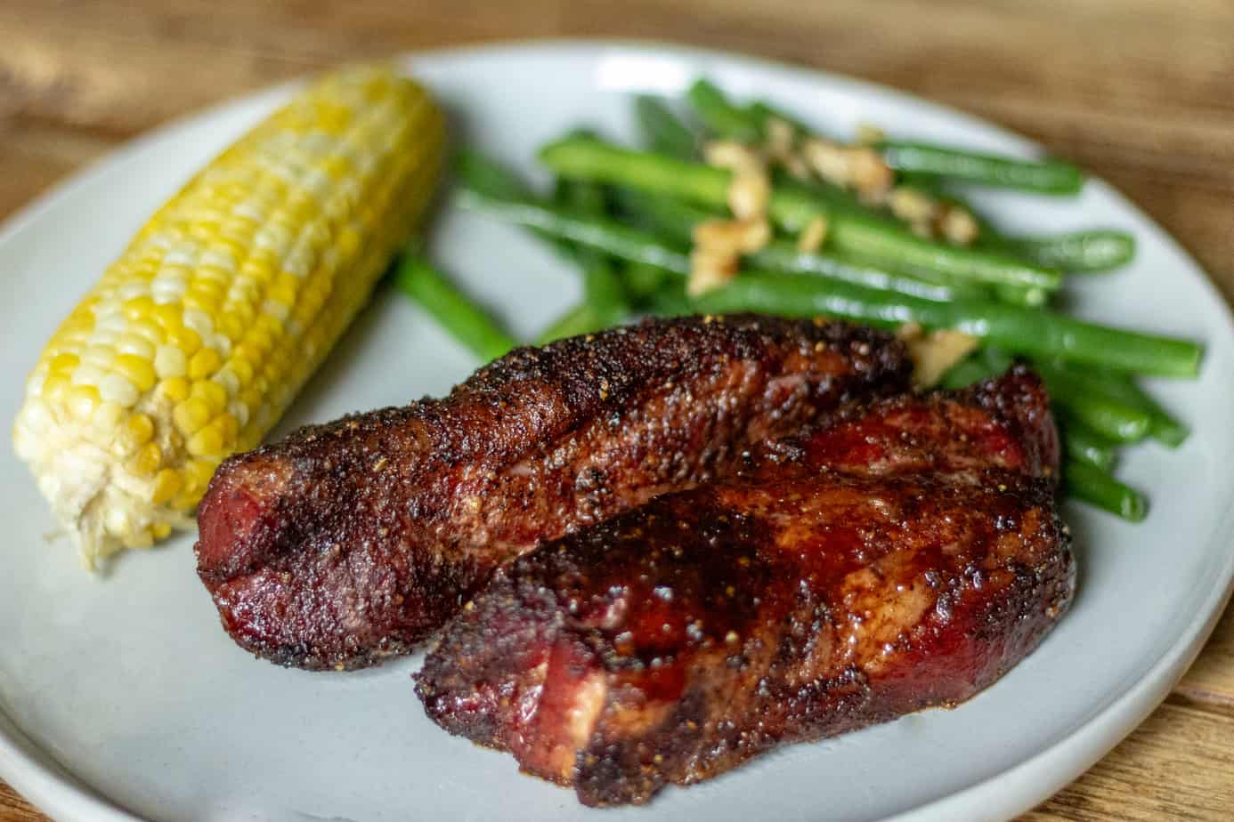 Two pieces of smoked country style ribs on a plate with smoked corn on the cobb, and green beans