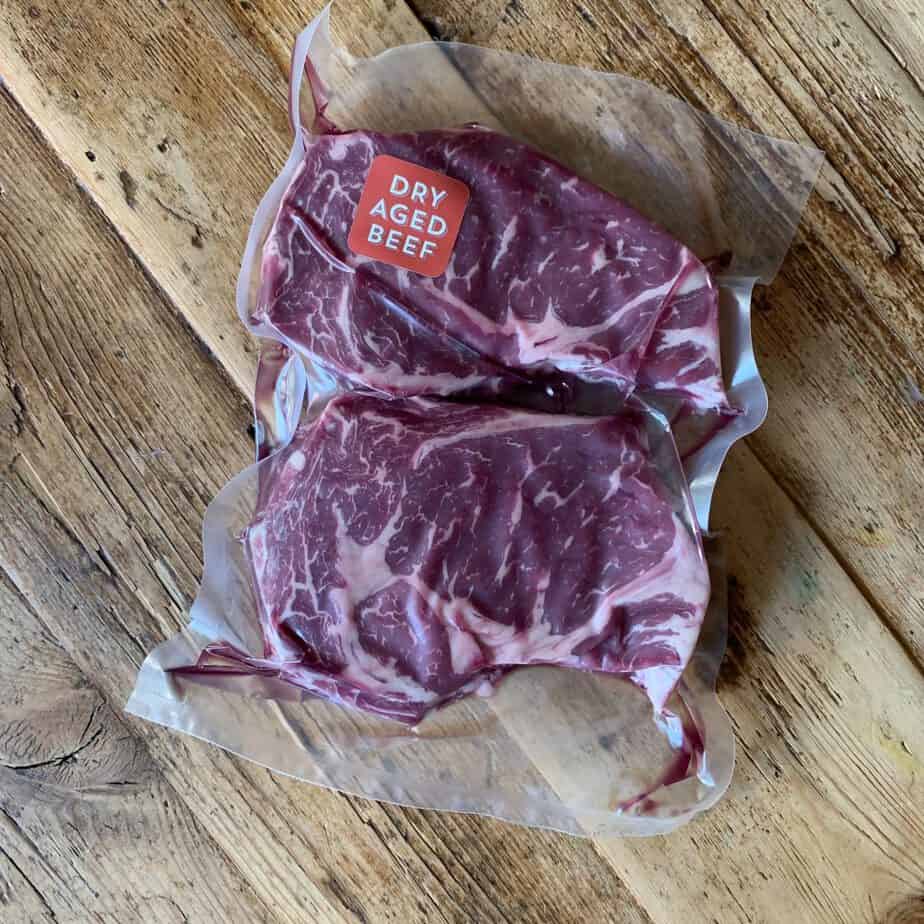 Two pack of dry aged ribeyes on a wood table