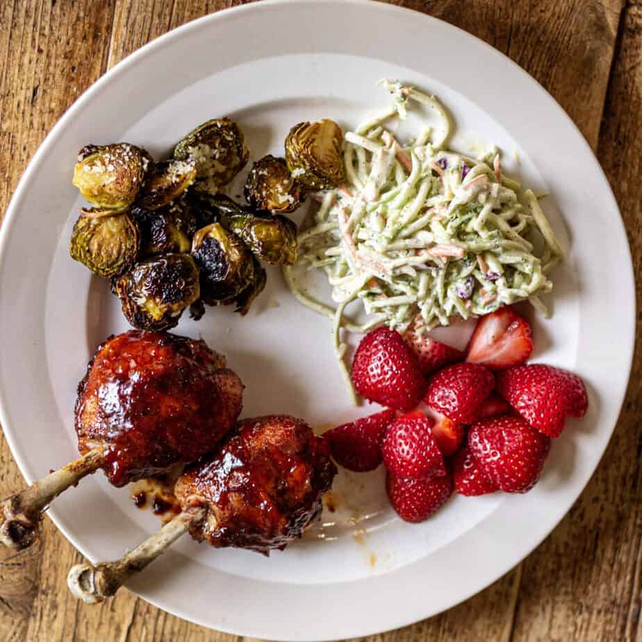 bbq chicken lollipops on a plate with cole slaw brussell sprouts and strawberries