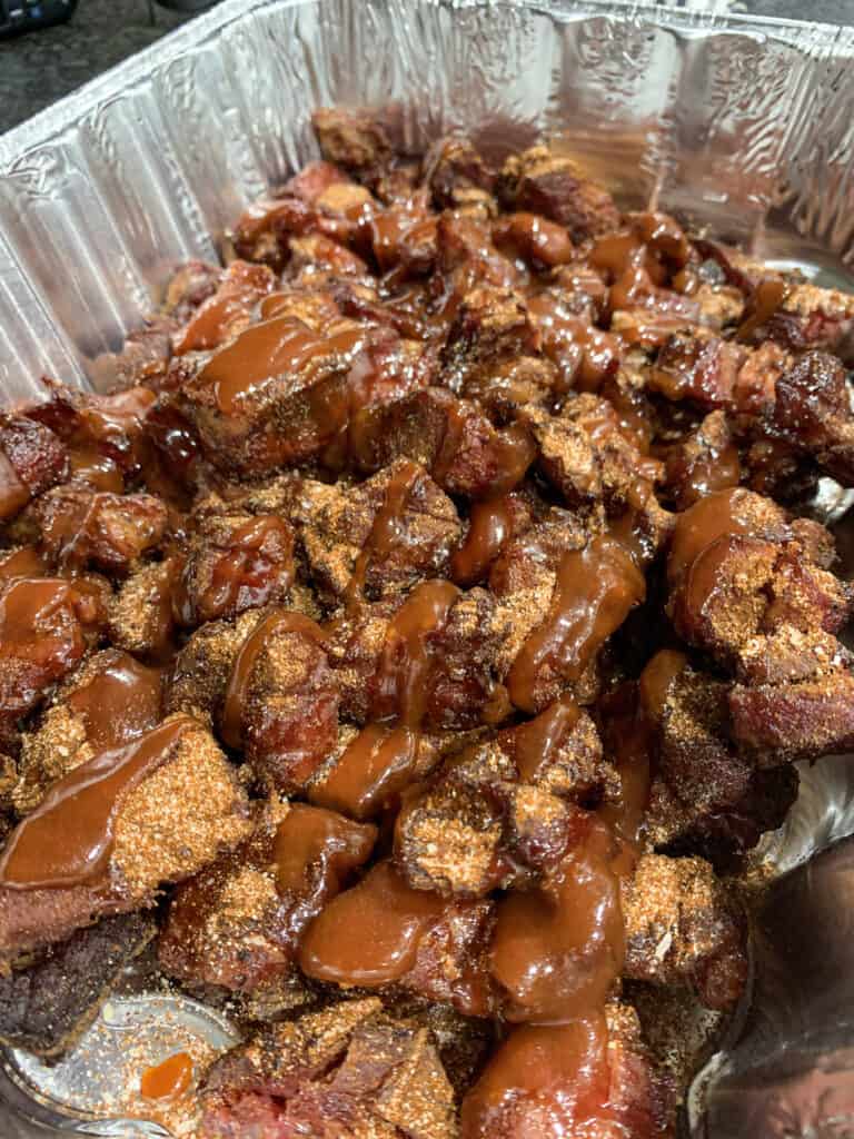 pork shoulder chunks in an aluminum pan with rub,, barbecue sauce, and honey