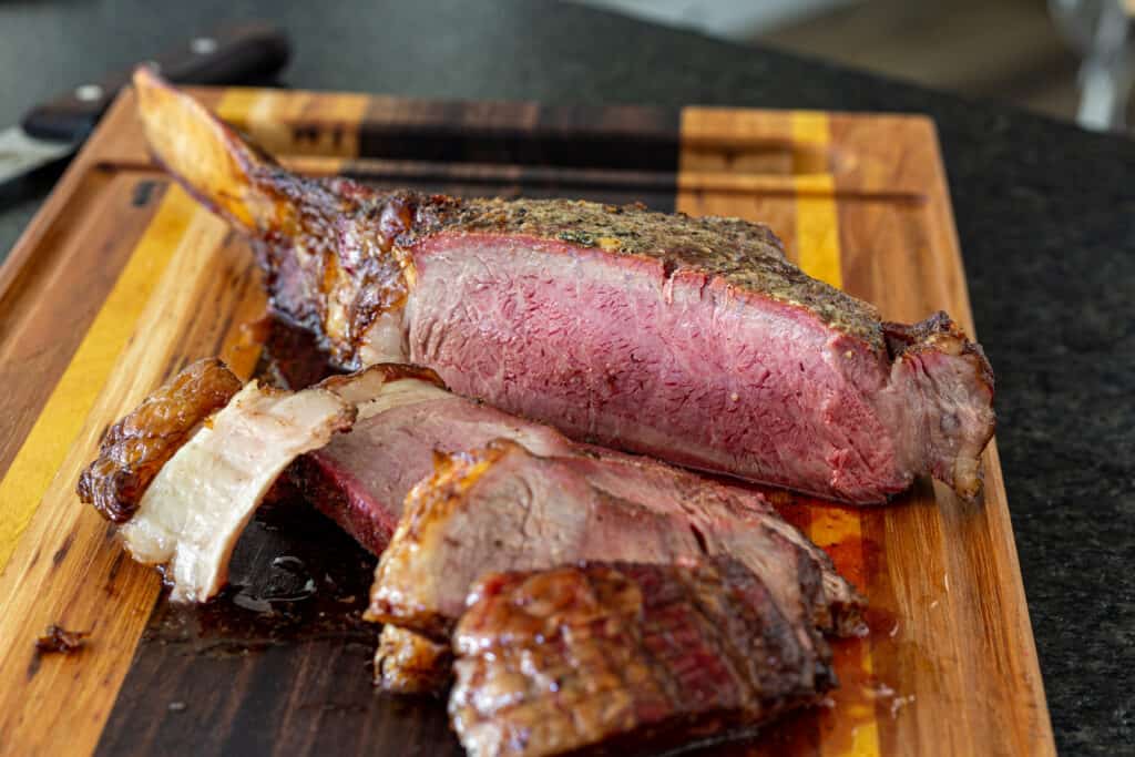 Sliced smoked tomahawk steak on a cutting board. The steak is medium rare and a smoke ring is present.