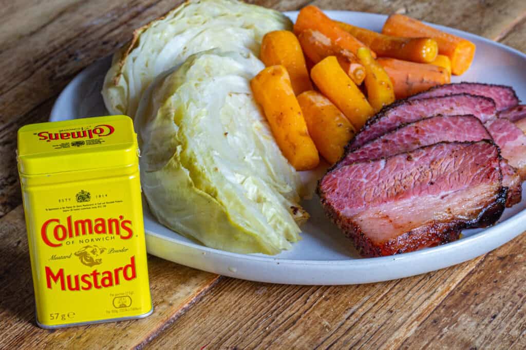 A Plate of Smoked Corned Beef Brisket, carrots, and cabbage with a container of Colman's Dry Mustard