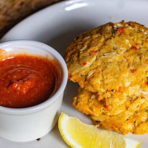 smoked crab cakes with a lemon and cocktail sauce on a white plate