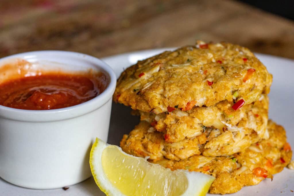 stack of smoked crab cakes with cocktail sauce and a lemon