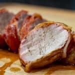 bacon wrapped pork tenderloin sliced on a cutting board