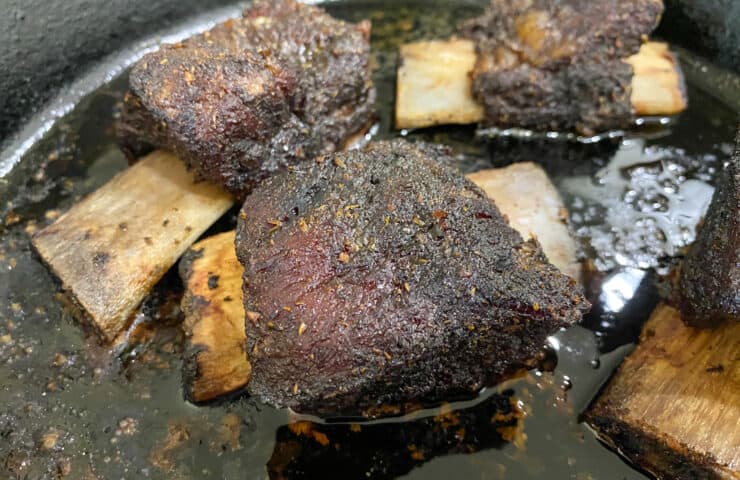 beef short ribs in a cast iron skillet on the smoker