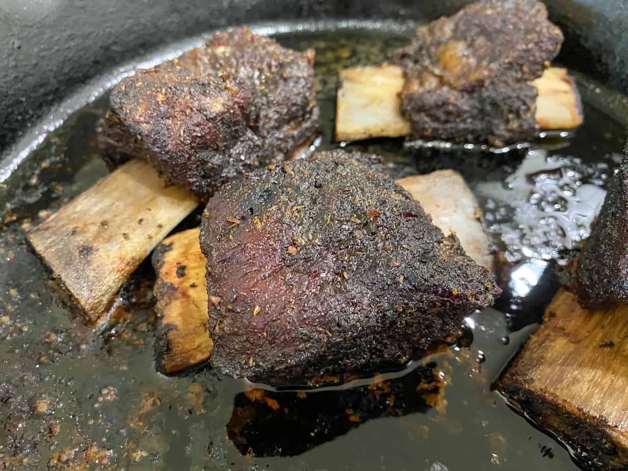 beef short ribs in a cast iron skillet on the smoker