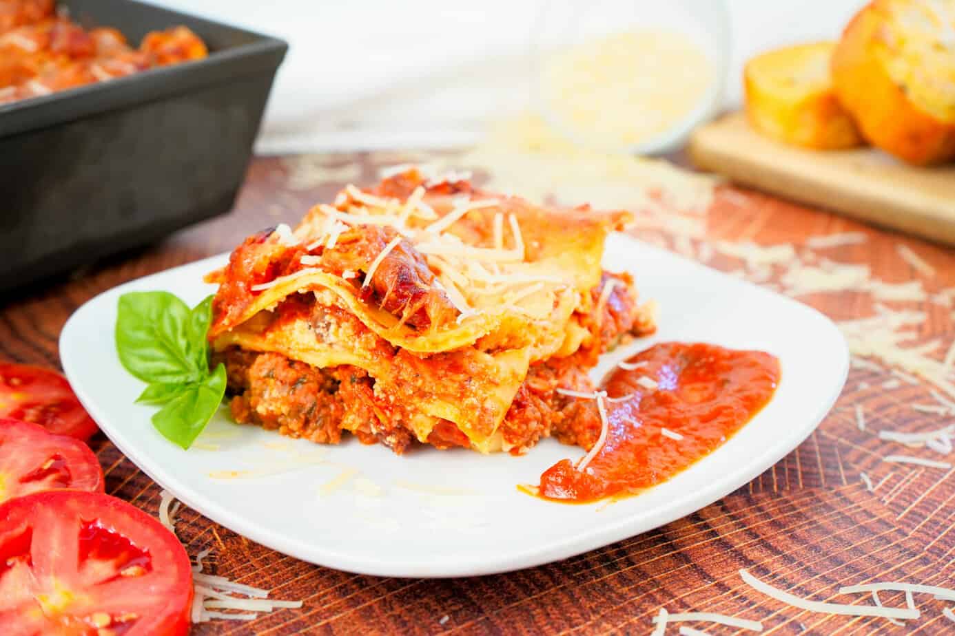 piece of lasagna on white plate with basil.