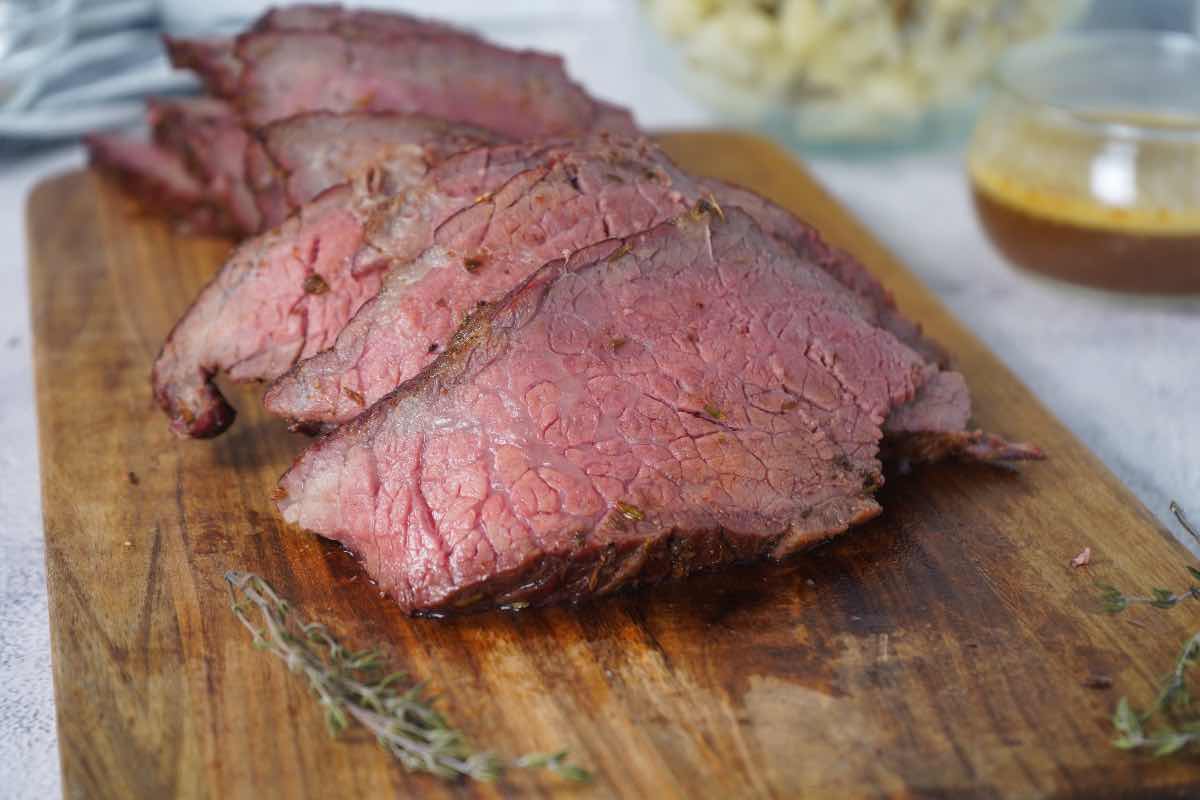 Smoked rump roast sliced with au jus behind and fresh thyme sprigs around it.