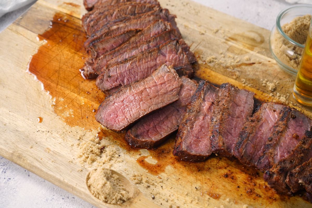 Smoked London Broil slices on cutting board with brown sugar and bourbon.
